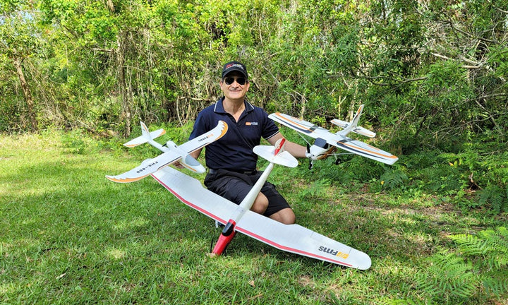 Man kneels in grass with three FMS RC planes, demonstrating different wing shapes for a STEM lesson