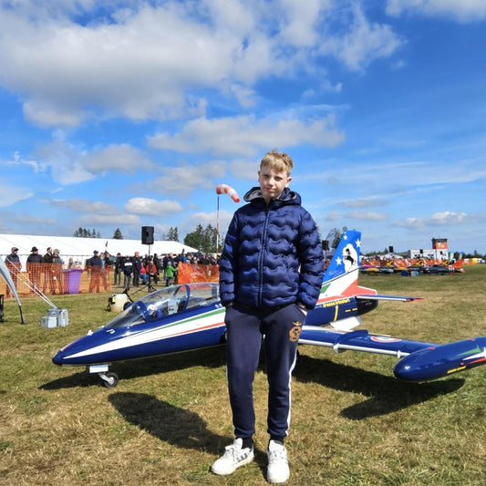 Jacopo Russo stands proudly with his sleek FMS RC Airplane at a sunny outdoor aviation event