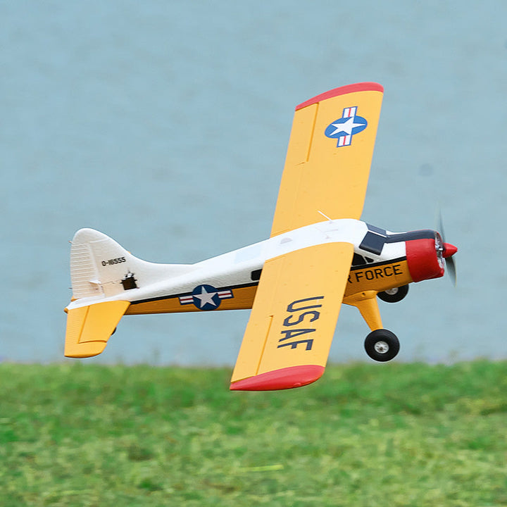 A yellow and white model airplane with "USAF" markings flying over green grass.