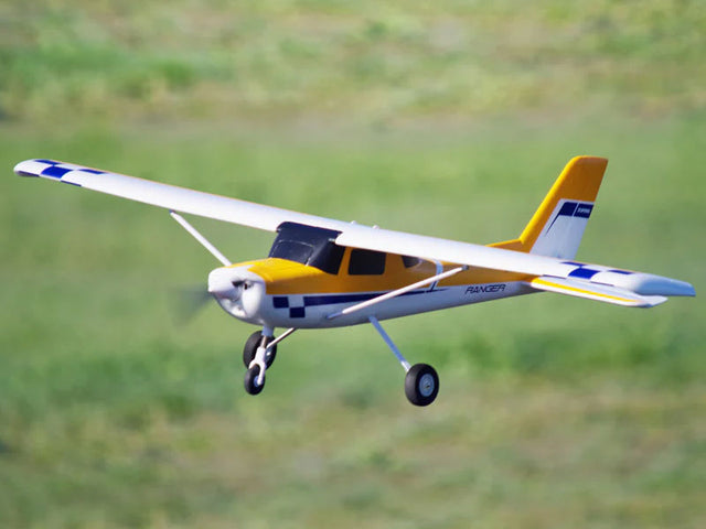 Yellow and white FMS Ranger RC plane flying low over a green field