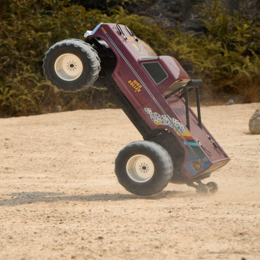 FMS RC Monster Truck performs a high-angle wheelie on sand, showcasing its "High Roller" dice graphics and power