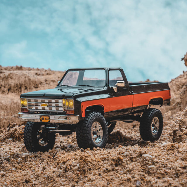 A heavily modified off-road pickup truck navigating through a rugged, sandy environment.