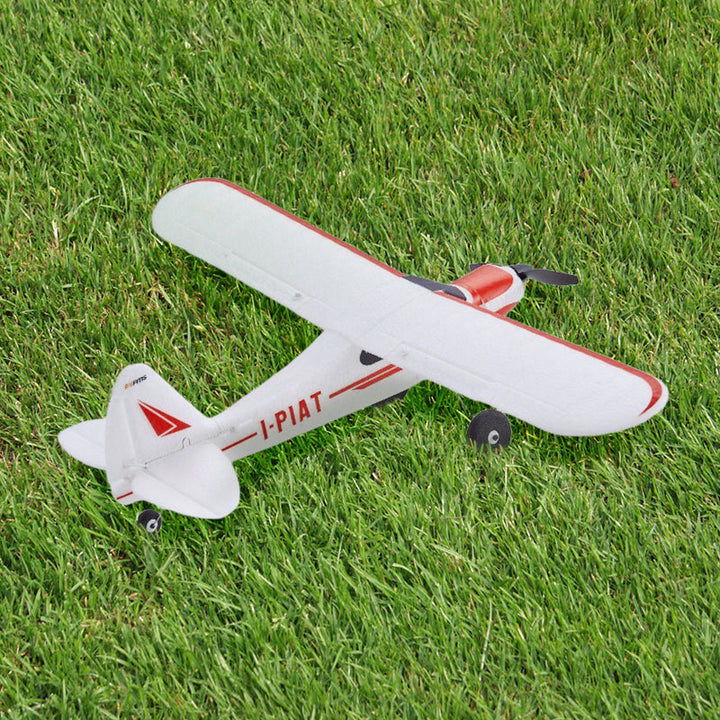 A red and white FMS RC Plane rests on a lush green grass field