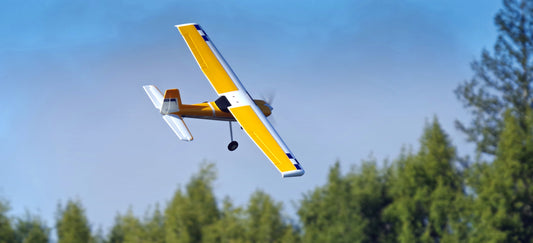 yellow and white RC trainer plane flying over trees
