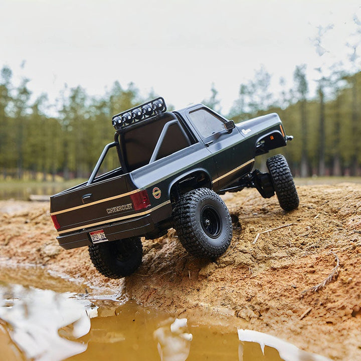 RC Chevrolet K10 climbing dirt hill near water.