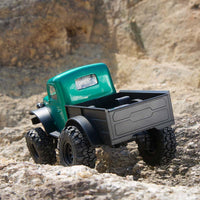 FMS 1:24 FCX24 Power Wagon Brushless RTR, metallic green, with black cargo bed and tires, driving on rocky terrain.