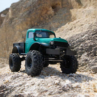 FMS 1:24 FCX24 Power Wagon Brushless RTR, metallic green RC truck with large off-road tires on rocky terrain.