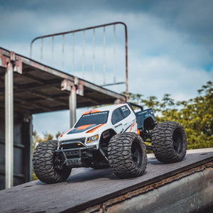 FMS 1:24 FMT24 Chevrolet Colorado monster truck RTR, white with orange accents, large tires, on a ramp.