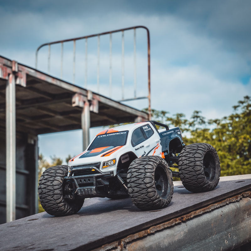 FMS 1:24 Chevrolet Colorado Monster Truck RTR on rugged terrain, featuring black oversized tires