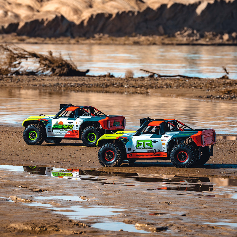 Two off-road vehicles on a muddy terrain with water in the background