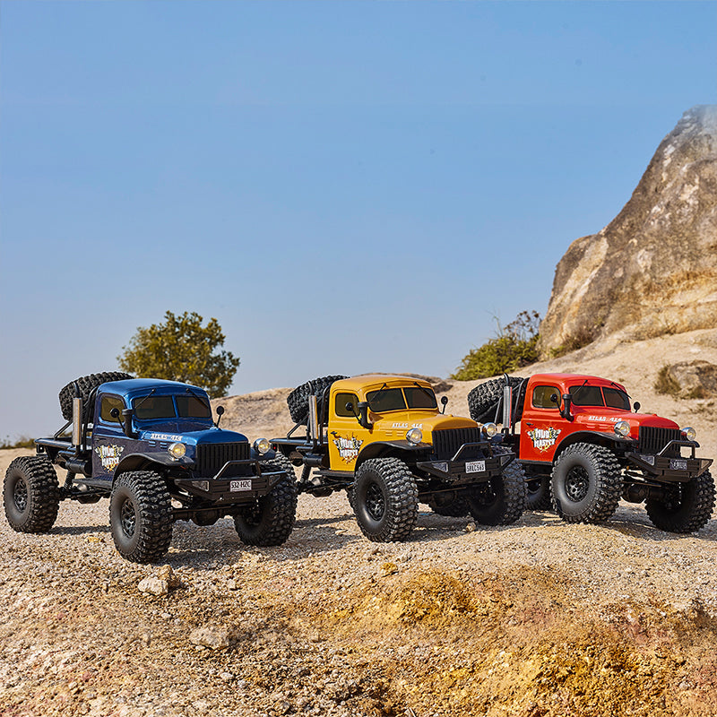 Three colorful RC off-road trucks in blue, orange, and red on rocky ground