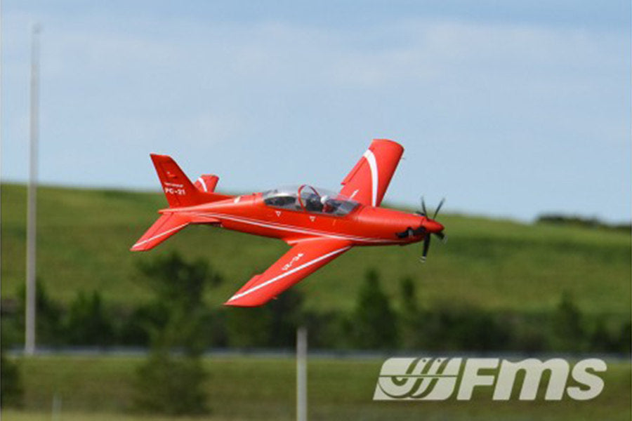 Red FMS 1100mm PC-21 Pilatus PNP RC airplane in flight with white accents and FMS logo.
