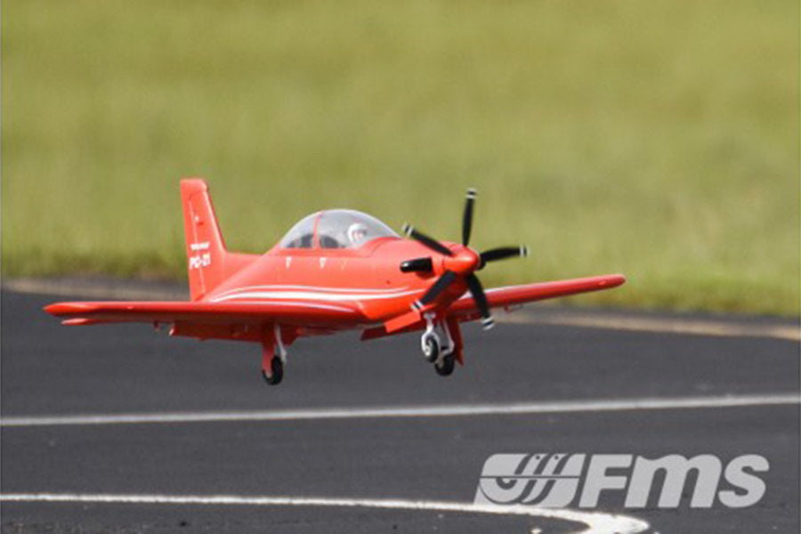 FMS 1100mm PC-21 Pilatus PNP RC plane in red with white trim, in flight over tarmac.